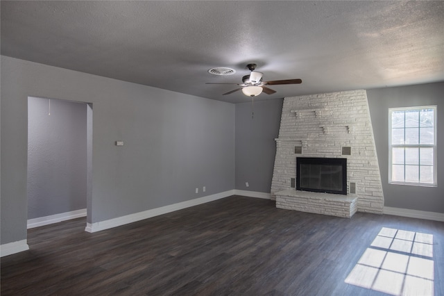 unfurnished living room featuring a large fireplace, wood-type flooring, a textured ceiling, ceiling fan, and brick wall