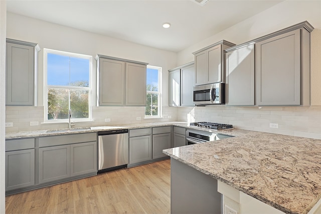 kitchen with sink, gray cabinets, appliances with stainless steel finishes, light stone countertops, and light wood-type flooring