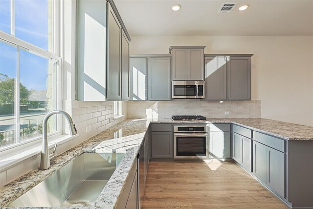 kitchen featuring sink, appliances with stainless steel finishes, light stone counters, decorative backsplash, and light wood-type flooring