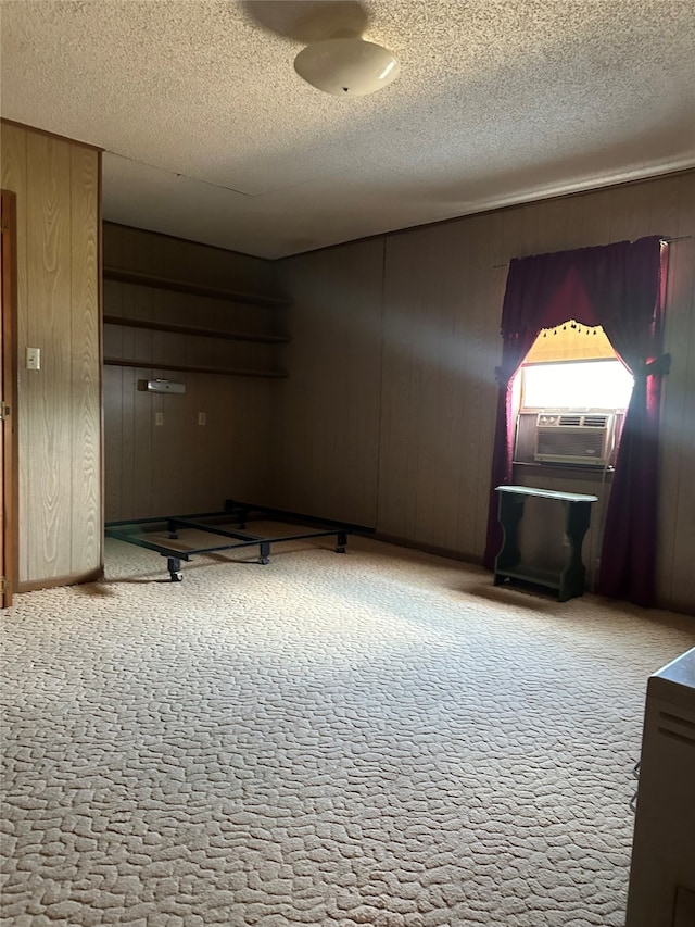 carpeted spare room with wood walls, a textured ceiling, and cooling unit