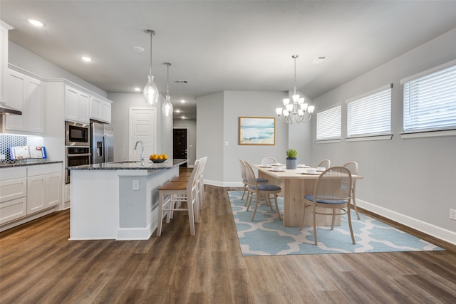 kitchen with a kitchen island with sink, stainless steel appliances, hanging light fixtures, and dark wood-type flooring