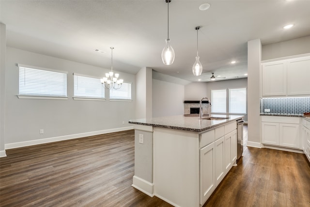 kitchen featuring ceiling fan with notable chandelier, white cabinets, a center island with sink, and dark wood-type flooring