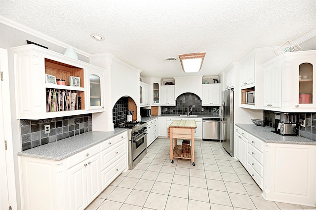 kitchen featuring light tile patterned floors, appliances with stainless steel finishes, backsplash, ornamental molding, and white cabinets