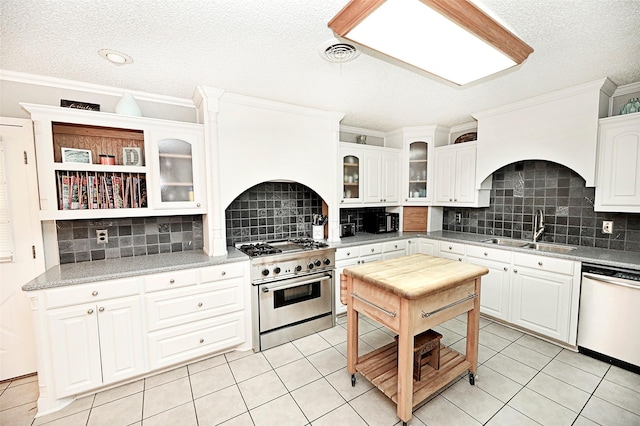 kitchen featuring sink, white cabinets, dishwashing machine, high end stainless steel range oven, and light tile patterned floors