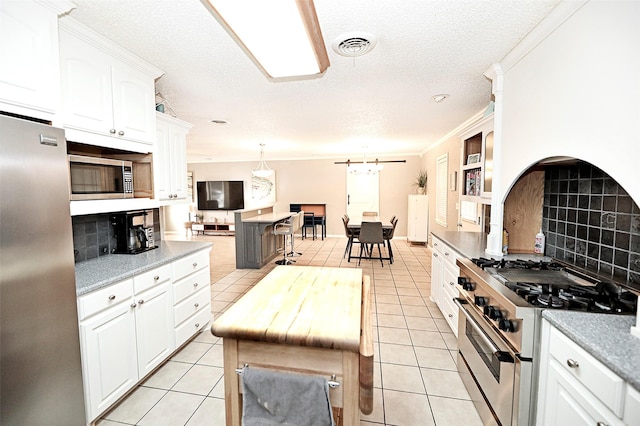 kitchen featuring appliances with stainless steel finishes, decorative light fixtures, light tile patterned floors, and white cabinets