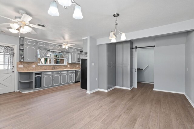 kitchen with gray cabinetry, a barn door, light hardwood / wood-style floors, ceiling fan, and tasteful backsplash