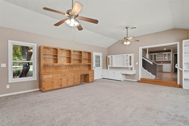 unfurnished living room with ceiling fan, carpet flooring, baseboards, vaulted ceiling, and built in study area