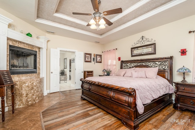 bedroom featuring hardwood / wood-style flooring, a raised ceiling, ceiling fan, and crown molding