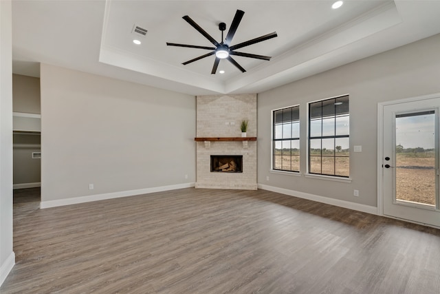 unfurnished living room with a fireplace, wood-type flooring, ceiling fan, a raised ceiling, and crown molding