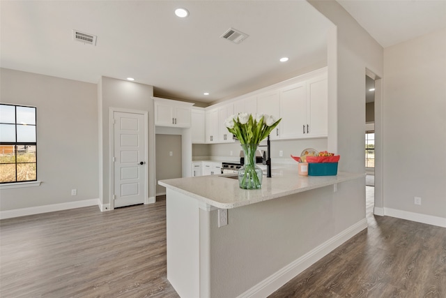 kitchen with kitchen peninsula, dark wood-type flooring, white cabinets, and a wealth of natural light