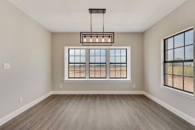 spare room featuring dark hardwood / wood-style floors, an inviting chandelier, and a healthy amount of sunlight