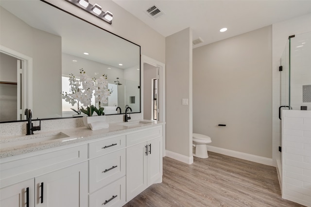 bathroom featuring toilet, an enclosed shower, double sink vanity, and wood-type flooring