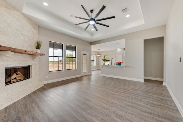 unfurnished living room featuring ceiling fan, a raised ceiling, a brick fireplace, and hardwood / wood-style floors