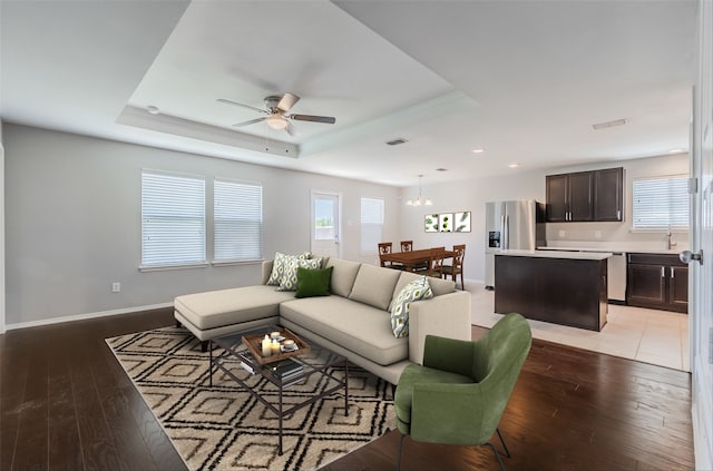 living room with ceiling fan with notable chandelier, a tray ceiling, and wood-type flooring