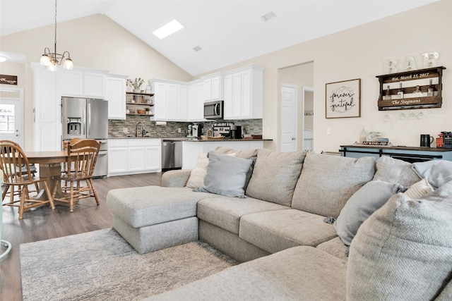 living room with hardwood / wood-style flooring, an inviting chandelier, high vaulted ceiling, and sink