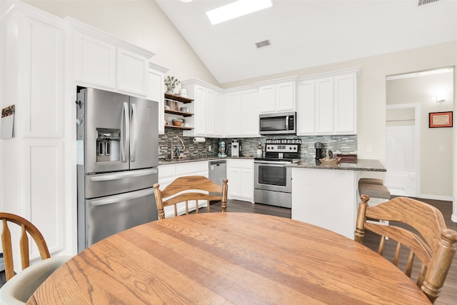 kitchen with appliances with stainless steel finishes, vaulted ceiling, white cabinets, and tasteful backsplash