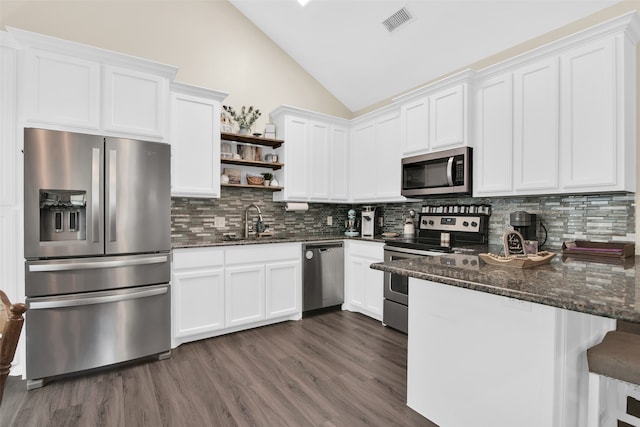 kitchen featuring backsplash, stainless steel appliances, dark stone counters, kitchen peninsula, and dark wood-type flooring