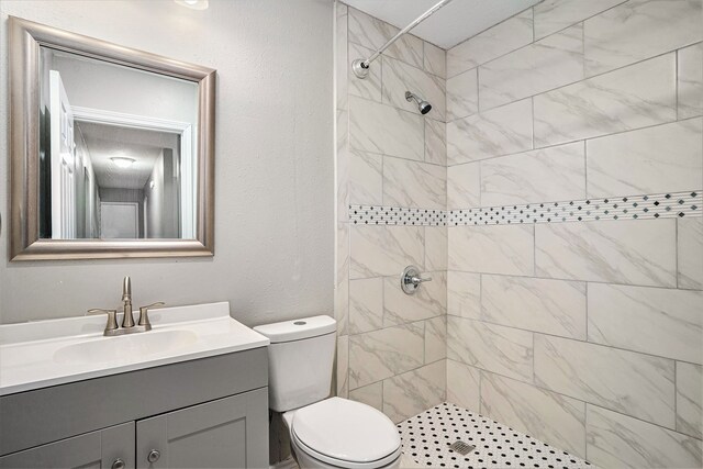 bathroom with tiled shower, toilet, and vanity