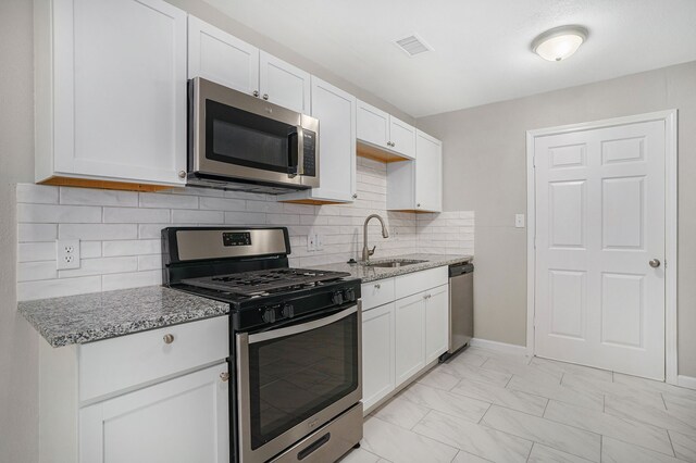 kitchen with appliances with stainless steel finishes, sink, decorative backsplash, and white cabinets