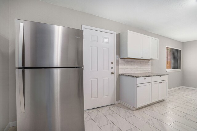 kitchen featuring tasteful backsplash, white cabinets, stainless steel refrigerator, light stone counters, and light tile patterned floors