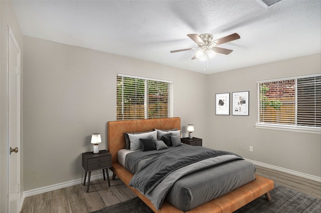 bedroom with a textured ceiling, ceiling fan, multiple windows, and hardwood / wood-style flooring