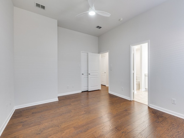 unfurnished bedroom with ceiling fan, connected bathroom, and dark wood-type flooring