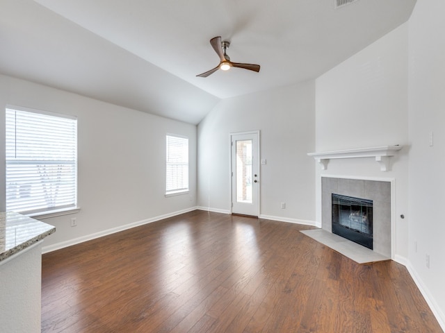 unfurnished living room featuring hardwood / wood-style flooring, vaulted ceiling, a tiled fireplace, and ceiling fan