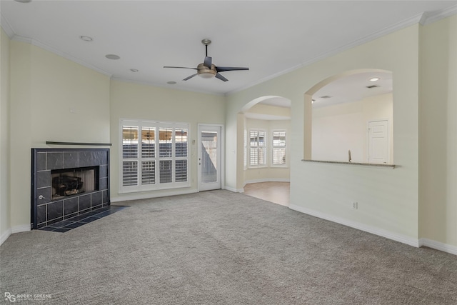 unfurnished living room featuring ornamental molding, a tile fireplace, ceiling fan, and dark colored carpet