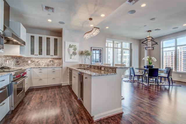 kitchen featuring hanging light fixtures, high end stainless steel range, white cabinets, wall chimney exhaust hood, and sink