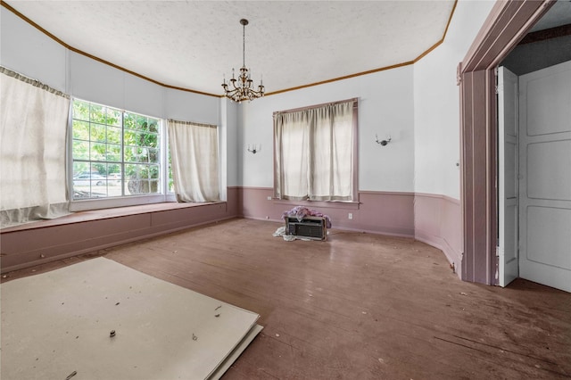 empty room featuring a textured ceiling, hardwood / wood-style flooring, crown molding, and a notable chandelier