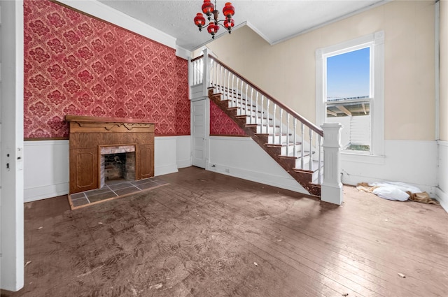 unfurnished living room featuring a notable chandelier, a textured ceiling, a tiled fireplace, dark hardwood / wood-style flooring, and ornamental molding