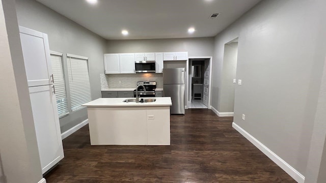 kitchen featuring dark hardwood / wood-style floors, backsplash, white cabinetry, appliances with stainless steel finishes, and a center island with sink