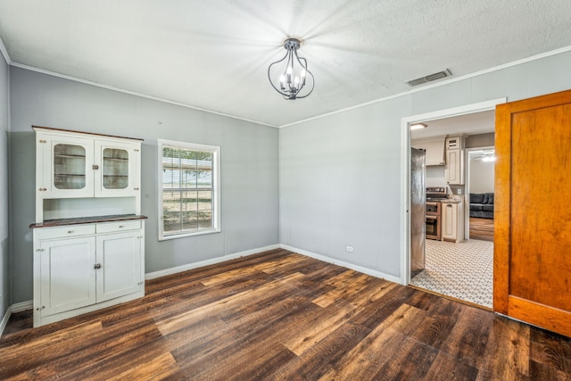 unfurnished dining area with a textured ceiling, a notable chandelier, dark tile patterned floors, and ornamental molding