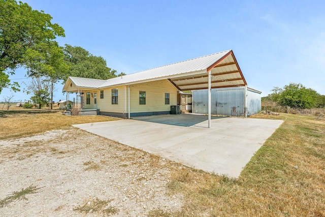 back of house with central air condition unit, a lawn, metal roof, a carport, and driveway