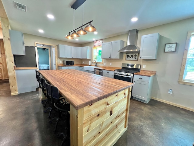 kitchen with appliances with stainless steel finishes, plenty of natural light, wall chimney range hood, and wooden counters