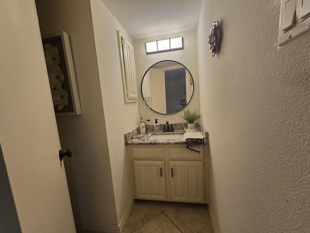 bathroom featuring a textured ceiling, a textured wall, tile patterned flooring, vanity, and baseboards