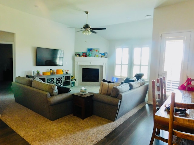 living room with ceiling fan, vaulted ceiling, a brick fireplace, and dark wood-type flooring