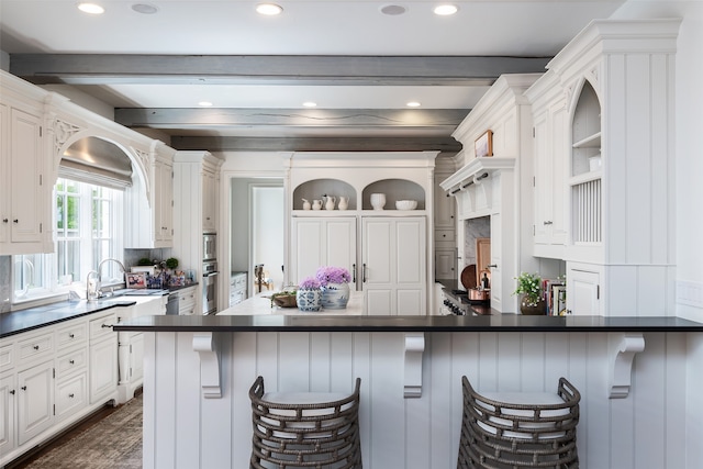 kitchen with a kitchen breakfast bar, beamed ceiling, white cabinetry, and dark hardwood / wood-style floors