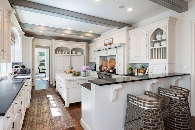 kitchen with a kitchen breakfast bar, beam ceiling, dark hardwood / wood-style floors, stainless steel range, and white cabinets