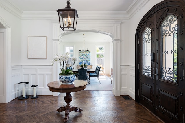 foyer entrance with ornamental molding, dark parquet floors, and a chandelier