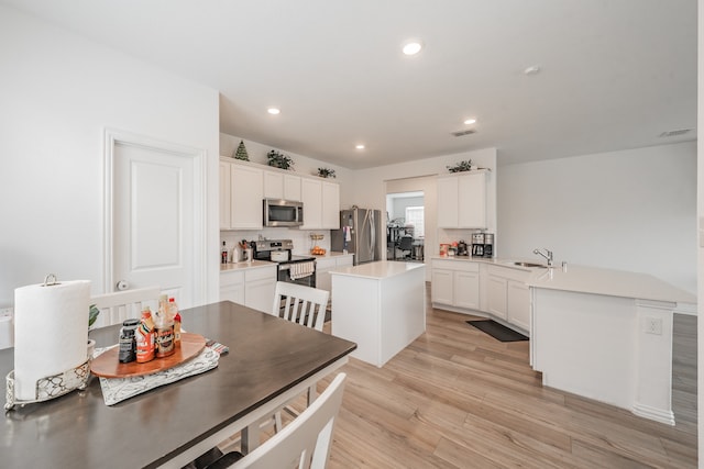 kitchen with stainless steel appliances, sink, light wood-type flooring, white cabinets, and a kitchen island