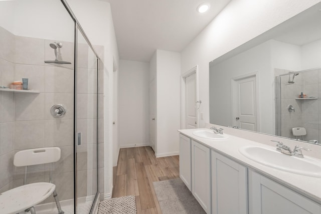 bathroom with a stall shower, wood finished floors, double vanity, and a sink