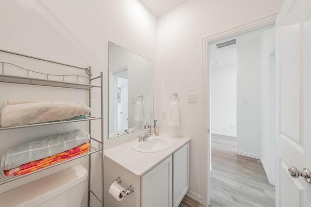 half bath featuring vanity, toilet, visible vents, baseboards, and wood finished floors