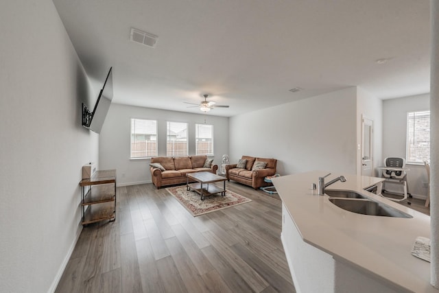 living room featuring a ceiling fan, visible vents, wood finished floors, and baseboards