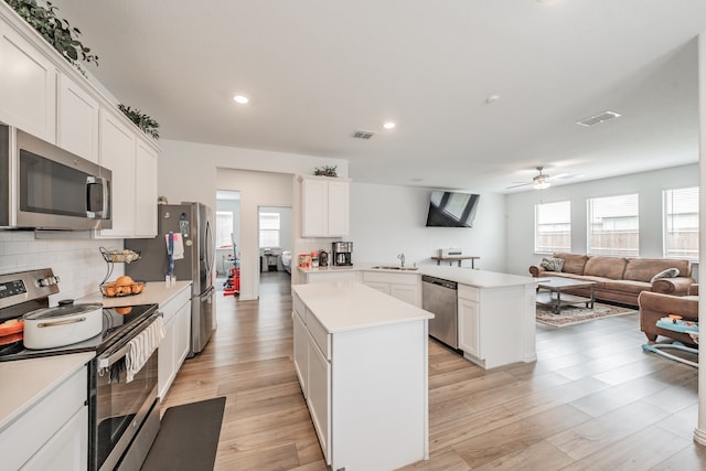 kitchen featuring appliances with stainless steel finishes, light hardwood / wood-style floors, tasteful backsplash, a kitchen island, and ceiling fan