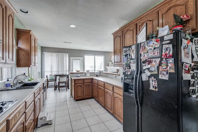 kitchen with sink, black fridge, a textured ceiling, light tile patterned floors, and kitchen peninsula