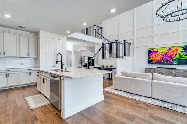 kitchen with white cabinetry, sink, hardwood / wood-style floors, stainless steel dishwasher, and an island with sink