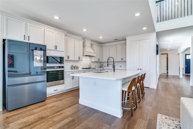 kitchen featuring stainless steel appliances, sink, white cabinetry, light hardwood / wood-style flooring, and premium range hood