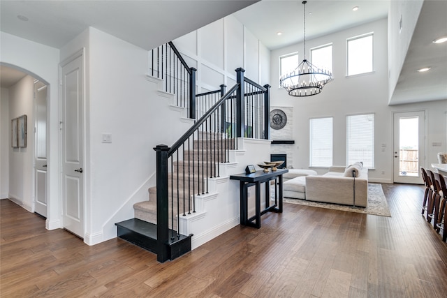 staircase with a chandelier, a towering ceiling, hardwood / wood-style flooring, and plenty of natural light