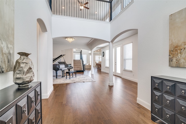 foyer entrance with dark wood-type flooring, a towering ceiling, ornate columns, and crown molding